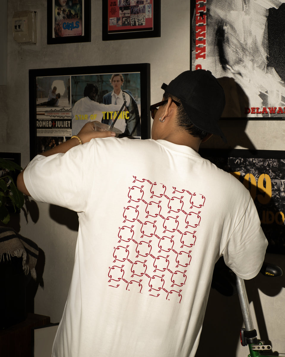 Person wearing a white t-shirt with a red geometric pattern, standing in a room with framed pictures on the wall.